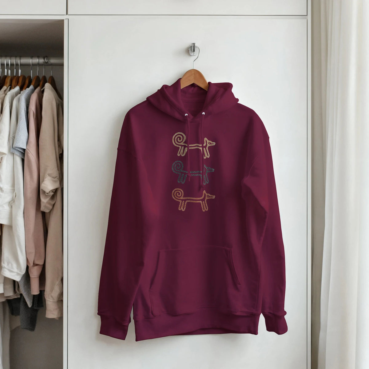 Maroon Dog Totem women's hoodie on a hanger by a clothes rail